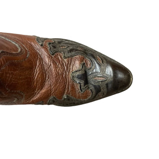 Brown leather cowboy boot with intricate designs on a wooden floor.