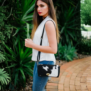 Woman holding a black and white cow print handbag in an outdoor setting