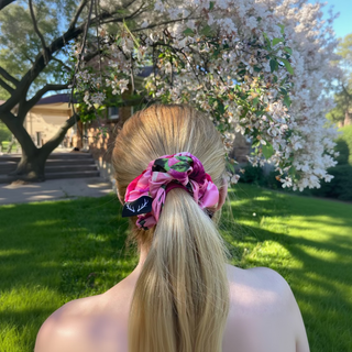 Person with a pink scrunchie in their hair standing in front of a flowering tree