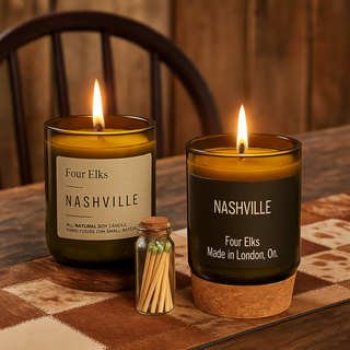 Two lit candles labeled 'Nashville' by Four Elks on a wooden table with a matchbox.