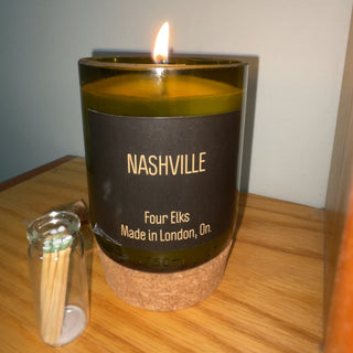 Candle in a glass container labeled 'Nashville' with matches on a wooden surface.