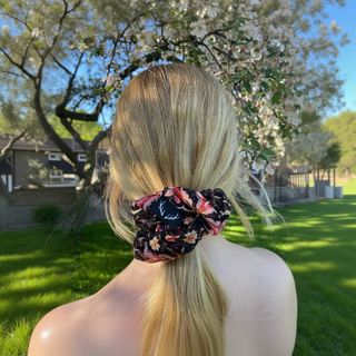 Person with a floral scrunchie in their hair, standing outdoors with trees in the background