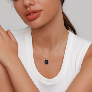 Woman wearing a gold necklace with a black pendant featuring a letter 'J' on a neutral background