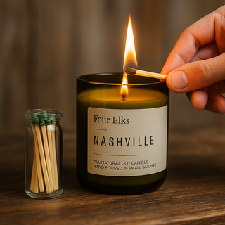 Hand lighting a 'Four Elks Nashville' candle with matches on a wooden surface.