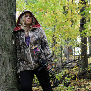 Woman in camouflage jacket holding a bow and arrow in a forest setting