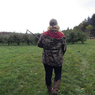 Person walking through an orchard holding a gun