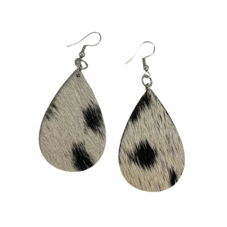 A pair of earrings featuring a cowhide pattern in black and white with a surgical steel backing.