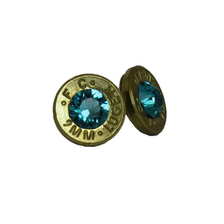 A pair of earrings made from recycled bullet casing with blue topaz stones, on a white background.