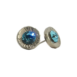 A pair of blue stud earrings made from recycled bullet casing with visible text on the metal, displayed against a white background.